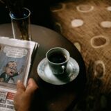 Ziar deschis și o ceașcă de cafea pe un birou, pregătite pentru lectura atentă a știrilor