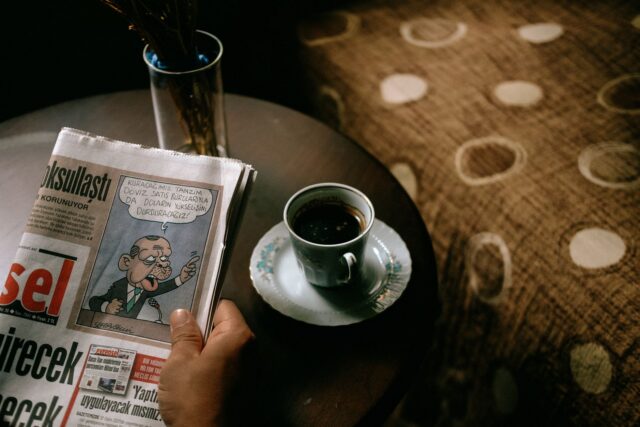 Ziar deschis și o ceașcă de cafea pe un birou, pregătite pentru lectura atentă a știrilor