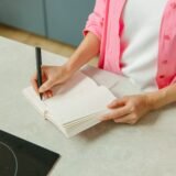 Caiet cu meniul săptămânii deschis pe blatul bucătăriei, lângă legume proaspete și o cană de ceai