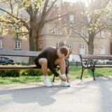 Alergător care își leagă șireturile pe o alee din parc, înaintea unui antrenament ușor